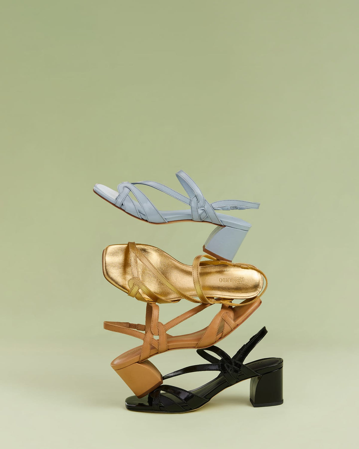 Three pairs of sandals in gold, black, and light blue on a light green background