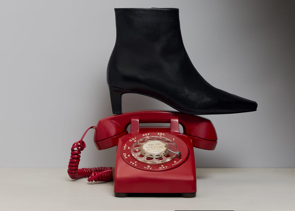 Everett Ankle Bootie in black leather resting on a red rotary phone